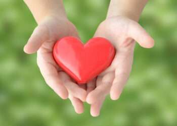 Child's hands covering heart object on natural green background
