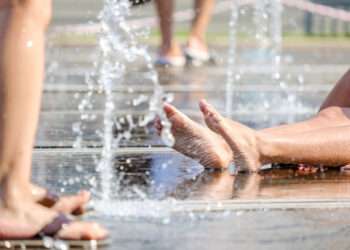 Beautiful legs of a girl sitting on the floor of a city fountain. Selective focus. Jets of cool water wash women's feet on a hot summer day.